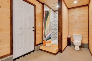 A wooden interior with a white door, a shower with a striped curtain, and a white toilet.