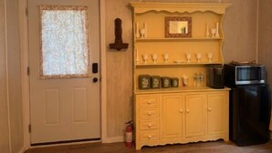 A room with a door, a wooden shelf with decorative items, a small cabinet, and a television. - Two cabins in one space. Enjoy your own private space in the cozy woods. Cabin is divided into two separate rooms. Dog friendly (Middle Grove)