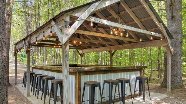 A rustic wooden bar with a metal railing and multiple stools. - Two cabins in one space. Enjoy your own private space in the cozy woods. Cabin is divided into two separate rooms. Dog friendly (Middle Grove)