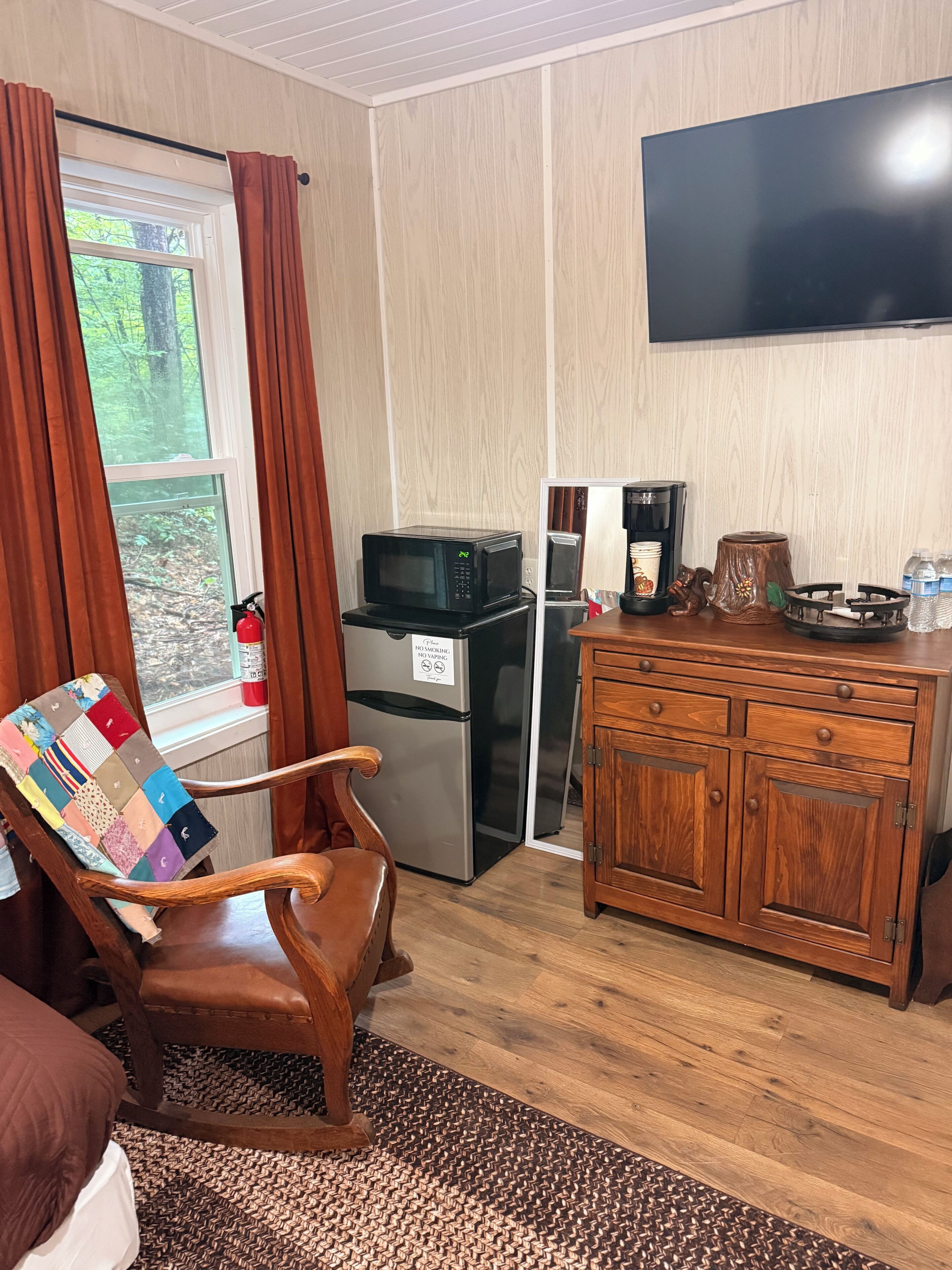 Een kamer met een houten stoel, een kleine koelkast, een magnetron, een koffiezetapparaat en een televisie aan de muur.