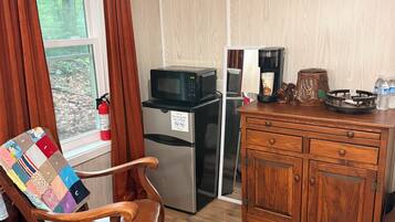 Een kamer met een houten stoel, een kleine koelkast, een magnetron, een koffiezetapparaat en een televisie aan de muur.