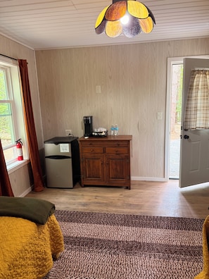 A room with a wooden cabinet, a coffee maker, and a fire extinguisher by the window.