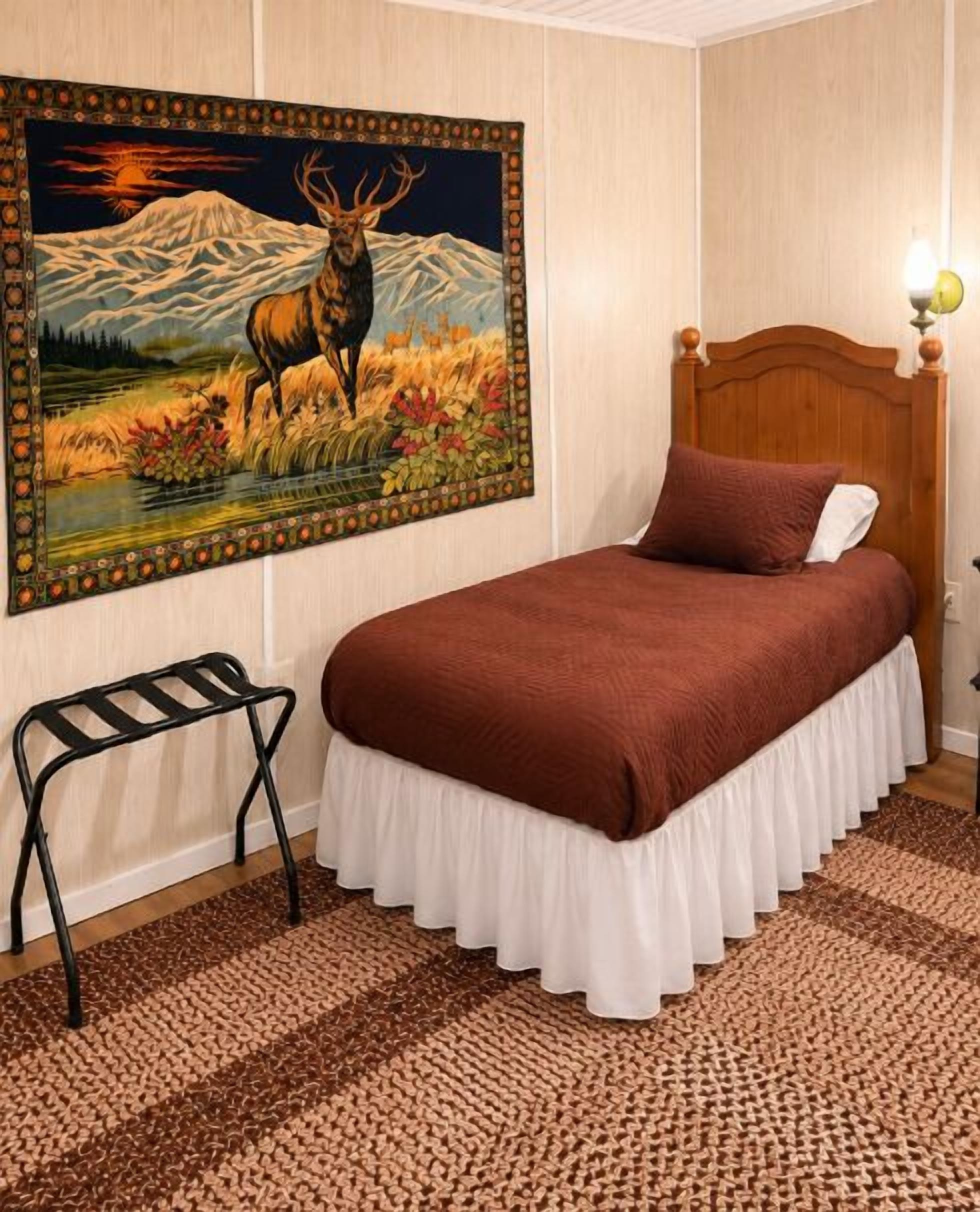 Un dormitorio con una cama, una mesita de noche, una lámpara, un cuadro de un ciervo y un cabecero de madera.