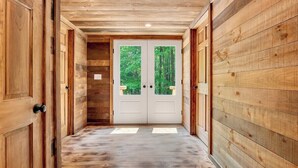 Un pasillo de madera que conduce a una puerta doble con vista al bosque.