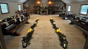 Un interior acogedor y rústico con chimenea de piedra, bancos de madera y un pasillo decorado festivamente con velas y follaje.