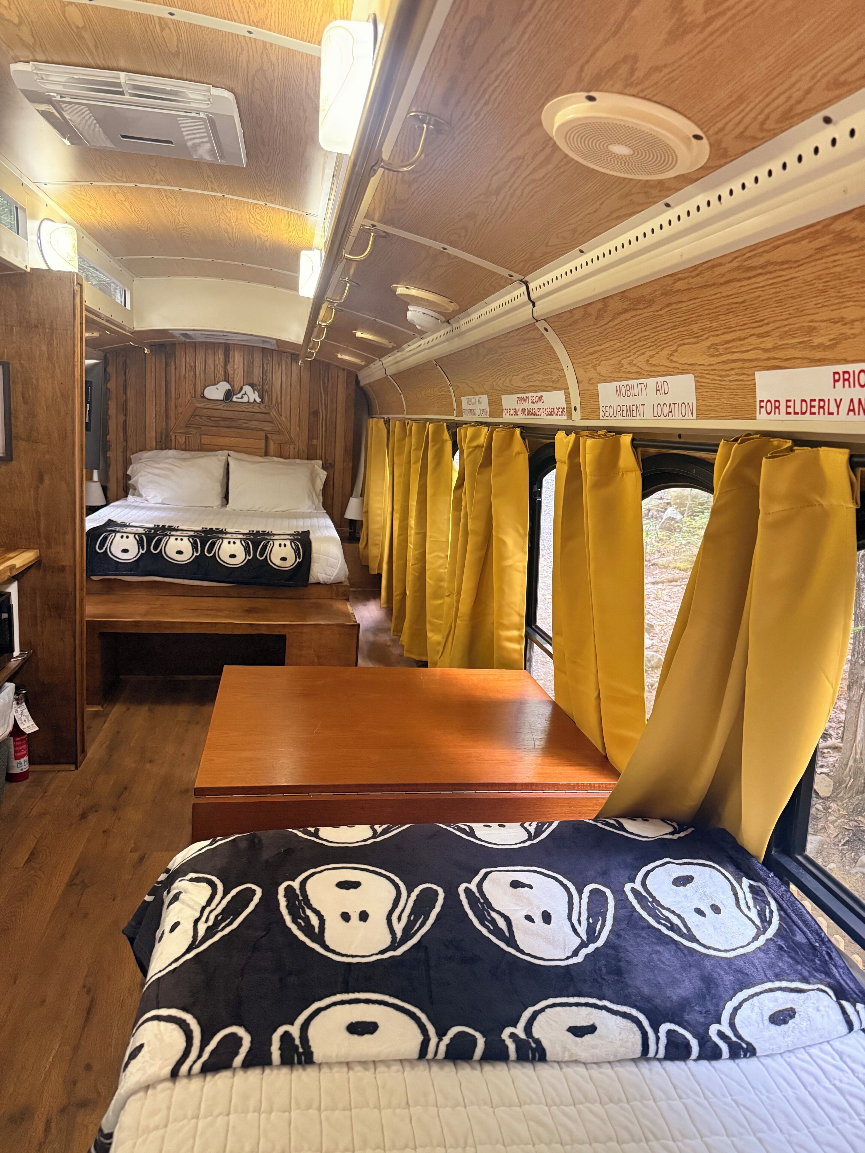 A train compartment with a bed, a table, yellow curtains, and signs indicating amenities like mobility aid and fruit serving.