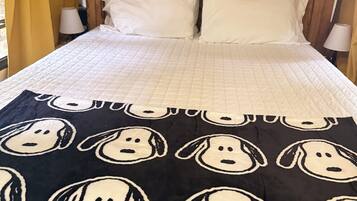 Un lit recouvert d’une couette blanche matelassée, une couverture noire ornée de motifs de chiens de dessins animés et une tête de lit en bois décorée avec un motif de Snoopy.