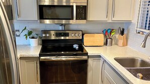 A compact kitchen with stainless steel appliances, including a microwave, oven, and refrigerator. - Artsy home near Downtown and Balboa Park (San Diego)