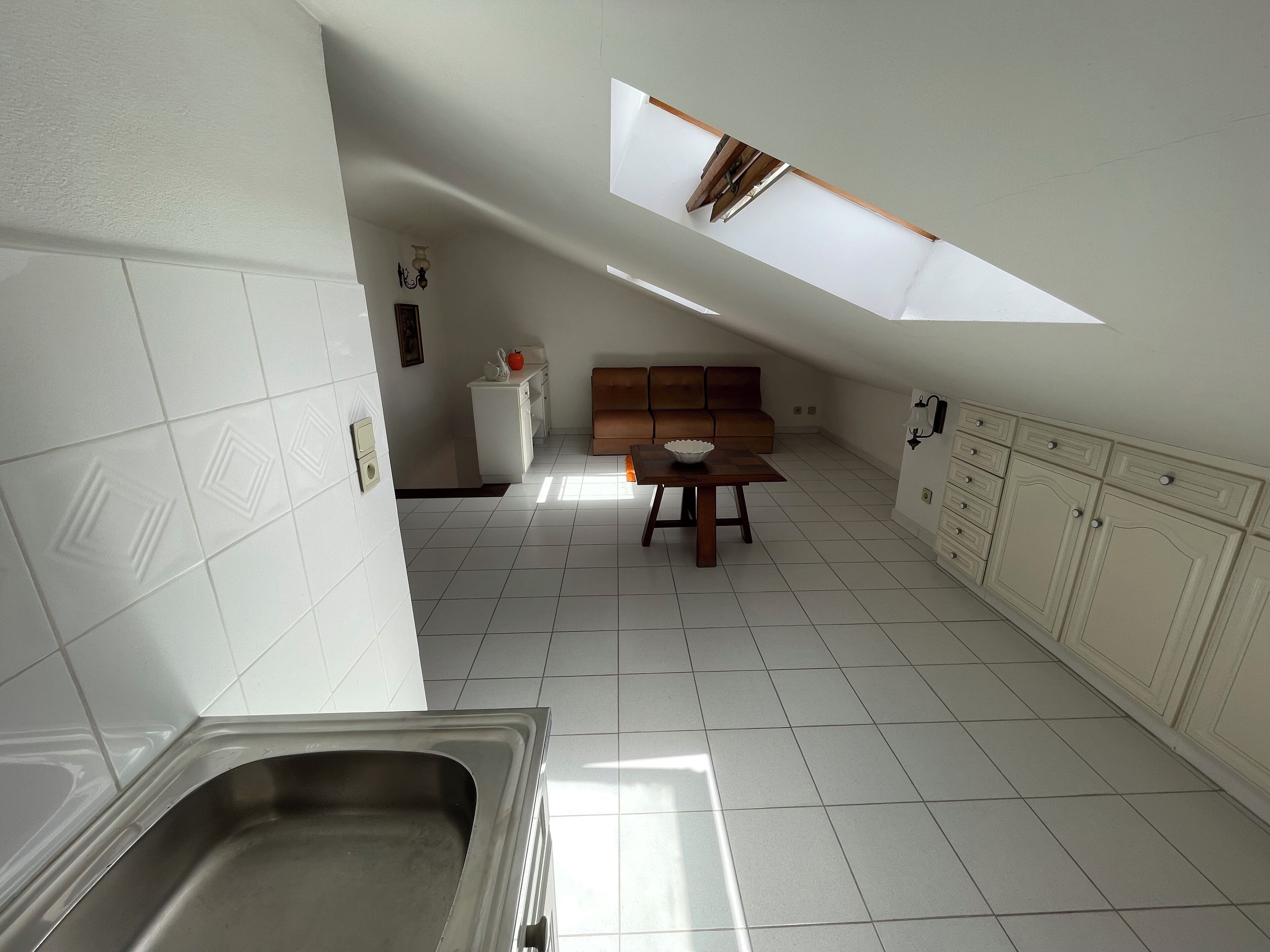 Una cucina con piastrelle bianche, un tavolo di legno, un forno integrato e una finestra sopra il lavello.