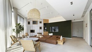 A modern living room with a brown leather sofa, a round dining table, wicker chairs, a large woven pendant light, and a green accent wall. - Elite Apartments Brzeźno Premium (Gdansk)