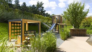 A wooden outdoor seating area with a slide, surrounded by greenery and a wooden deck. - Elite Apartments Brzeźno Premium (Gdansk)