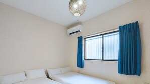 Ein Zimmer mit zwei Betten, einem Fenster mit blauen Vorhängen, einer Klimaanlage und einer Hängeleuchte.