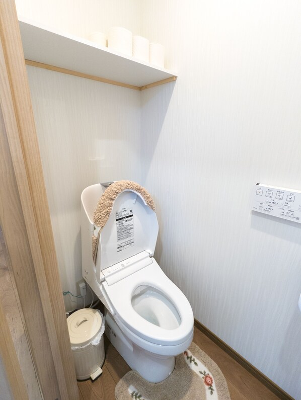 A white toilet with a beige seat cover, a white wall, and a wooden floor.