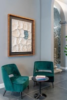 A modern interior with two teal chairs, a framed abstract artwork, and a small round table with books.