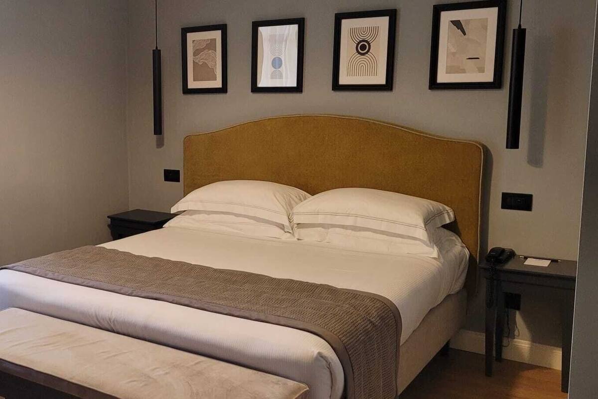 A neatly arranged bedroom with a bed, bedside tables, a bench, and framed artwork on the wall.