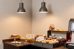 Un bufé de desayuno con diversas bollerías, una máquina de café y una selección de salsas.