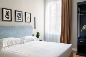 Un letto ben rifatto con lenzuola bianche, una testiera blu e tre opere d'arte astratte incorniciate appese al muro.