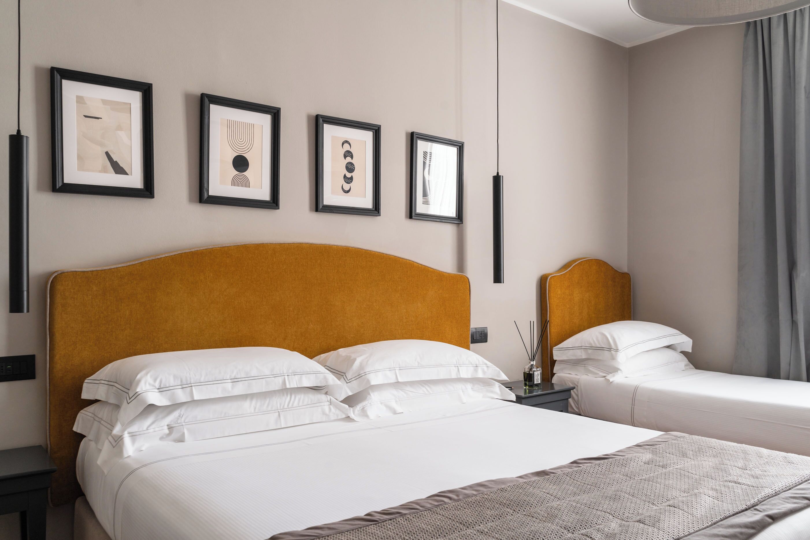 Habitación de hotel con una cama grande, una cama más pequeña y una mesita de noche con una lámpara. En la pared hay cuadros enmarcados.