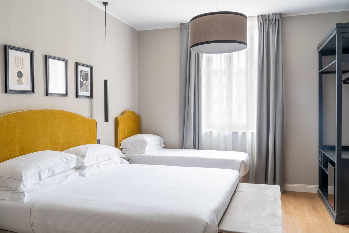 A hotel room with two beds, a wardrobe, and framed artwork on the wall.