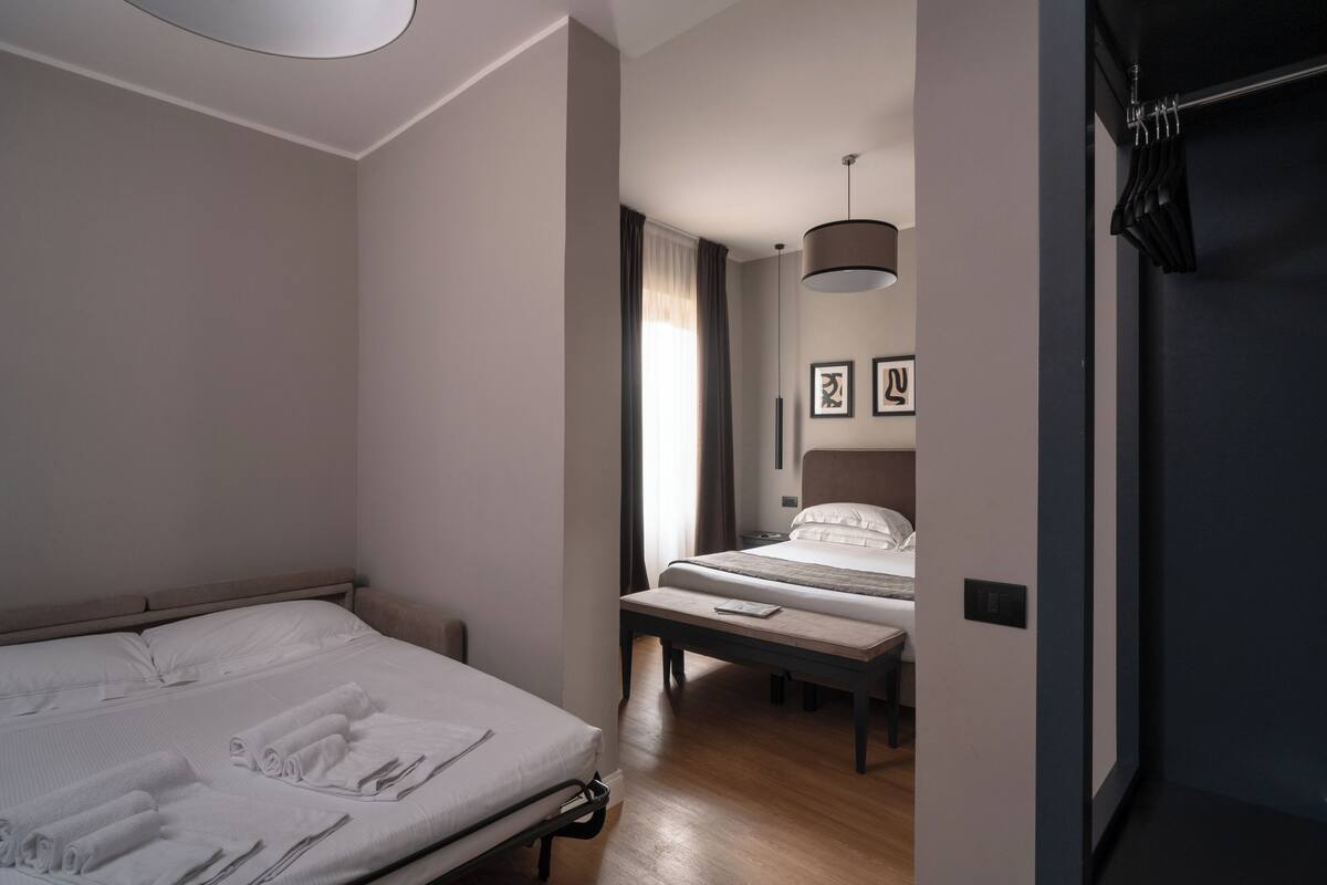 A hotel room with a large bed, a smaller bed, a desk, and a hanging light fixture.