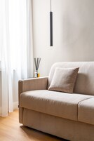Un divano beige con un cuscino, una lampada a sospensione nera e un diffusore di rattan su un tavolo.