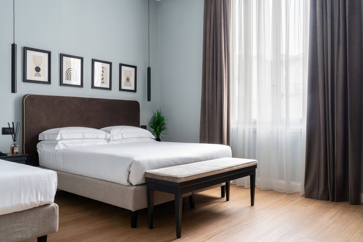 A modern bedroom with a large bed, a bench, and framed artwork on the wall.