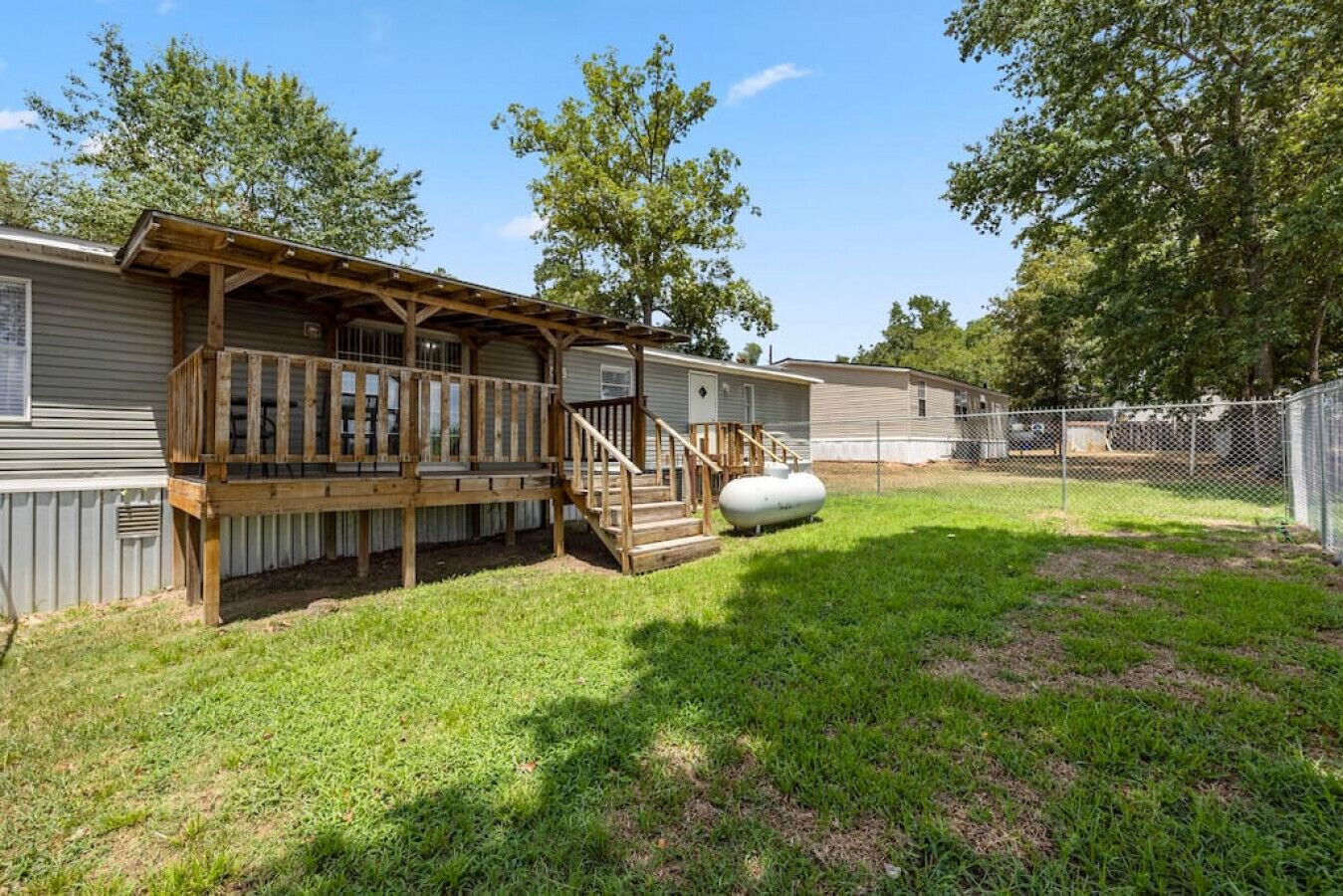 Une maison mobile dotée d’une terrasse en bois et d’une cour clôturée.