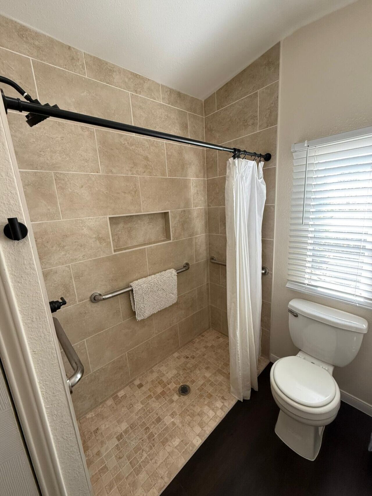 A bathroom with a shower, toilet, and window.