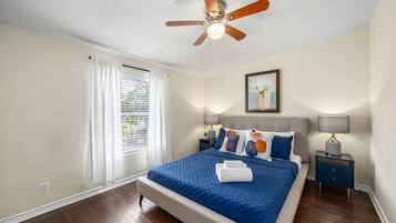 A bedroom with a bed, a ceiling fan, a nightstand, and a window with curtains.