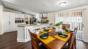 Une cuisine moderne avec des meubles blancs, un îlot central et un coin repas comprenant une table et des chaises en bois.