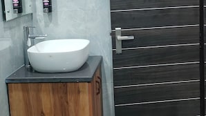 Un baño con lavamanos blanco, armario de madera y puerta oscura.