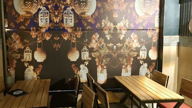 Un interior de restaurante con mesas y sillas de madera, faroles decorativos colgantes y arte floral en las paredes.