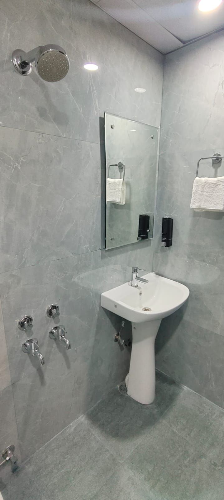 A modern bathroom with a glass-enclosed shower, a pedestal sink, and a wall-mounted mirror.