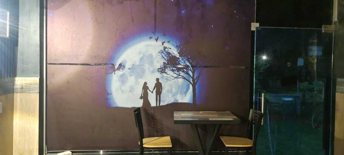 A restaurant with a mural of a couple holding hands under a full moon, a table, and two chairs.