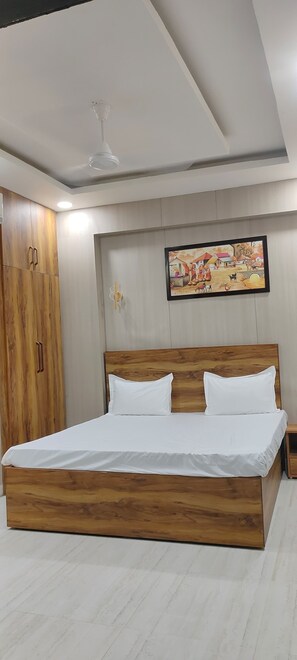 Una camera da letto con un letto in legno, biancheria da letto bianca, un armadio in legno e una ventola a soffitto.