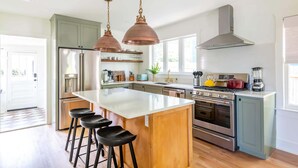 Une cuisine moderne dotée d’un îlot central, d’appareils électroménagers en acier inoxydable et de luminaires suspendus.