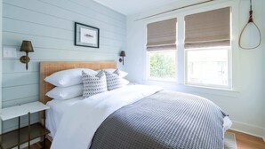 Une chambre à coucher avec un lit, des lampes de chevet, un tableau encadré et une fenêtre avec des stores.