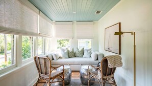 Une pièce chaleureuse avec un plafond bleu clair, un canapé blanc agrémenté de coussins, des fauteuils en osier et un lampadaire.