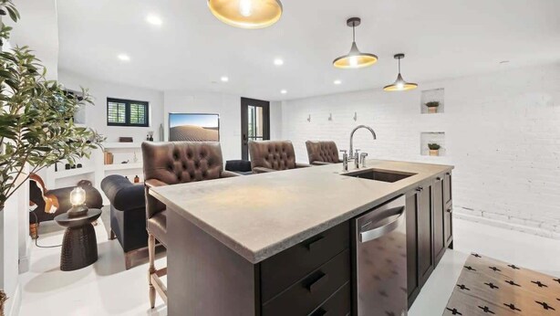 A modern kitchen with a central island, pendant lighting, and a white brick wall.