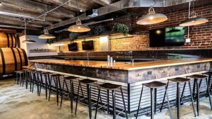 A bar area with a long counter, multiple stools, hanging lights, and a brick wall with a TV.