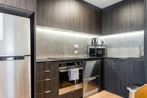 A modern kitchen with dark wood cabinetry, stainless steel appliances, and a black countertop.