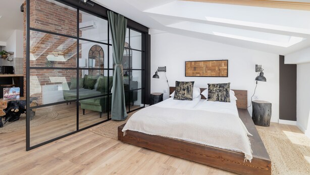 Un dormitorio moderno con una cama grande, un ventanal de vidrio que da a una sala de estar y un tragaluz.