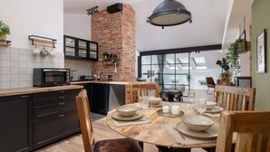 Una cocina moderna con pared de ladrillo, armarios negros y una mesa de comedor de madera dispuesta para cuatro.
