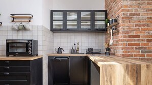 Una cocina compacta con lavavajillas integrado, microondas y cafetera. Hay armarios con puertas de cristal y un detalle de pared de ladrillo.