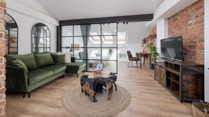 Una sala de estar moderna con un sofá verde, una mesa de centro con un perro, y un televisor en una pared de ladrillo.