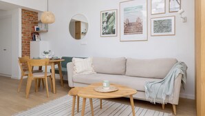 Un salon chaleureux avec un canapé, une table à manger et des chaises, une petite table basse ronde et un luminaire suspendu.