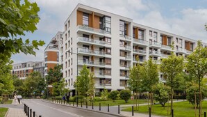 Een modern meerlaags woongebouw met balkons, een verharde straat en begroeiing.