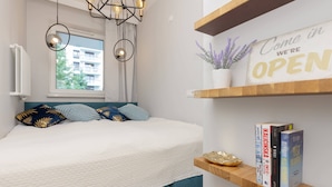 Een moderne slaapkamer met een bed, een raam, een bordje met de tekst 'We're Open' en boeken op een plank.