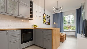 Een moderne keuken met grijze kastjes, een houten aanrechtblad en een zwarte oven. Er is een raam met blauwe gordijnen en een uitzicht op gebouwen.