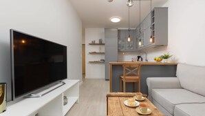 Een moderne woonkamer met een flatscreen-tv, een houten salontafel met borden en bekers, een grijze bank en een keukenhoek met kastjes en een spoelbak.